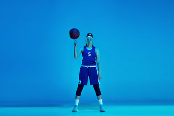 Wall Mural - Young caucasian female basketball player of team posing confident with ball isolated on blue background in neon light. Concept of sport, movement, energy and dynamic, healthy lifestyle. Training.