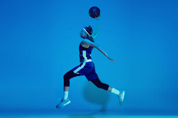 Wall Mural - Leader. Young caucasian female basketball player training, prcticing with ball isolated on blue background in neon light. Concept of sport, movement, energy and dynamic, healthy lifestyle.