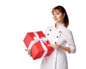 Portrait of young red-haired woman doctor or nurse in white medical gown demonstrating big present box with ribbon