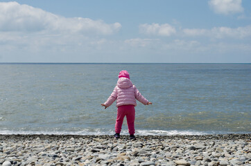 little girl on a stone beach at sea in spring