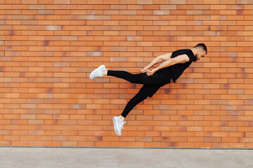 Full length of handsome young man in sport clothing jumping while exercising outside. Dynamic movement. Side view. Sport and healthy lifestyle. City, brick wall background.