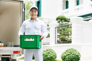 Wall Mural - Horizontal medium long portrait shot of modern milkman wearing white clothes standing outdoors holding plastic box with milk bottles, copy space