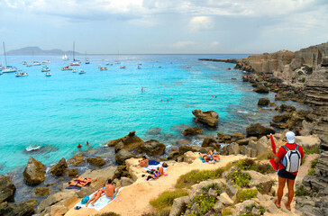 Wall Mural - paradise clear torquoise blue water with boats and cloudy blue sky in background in Favignana island, Cala Rossa Beach, Sicily South Italy.