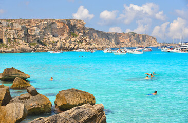 Wall Mural - paradise clear torquoise blue water with boats and cloudy blue sky in background in Favignana island, Cala Rossa Beach, Sicily South Italy.