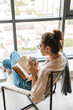 © Drobot Dean - Image of thinking cute woman reading book and drinking coffee