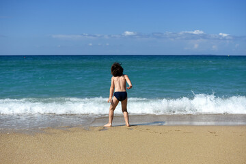 Wall Mural - Little boy enjoying on beach. Child sit on beach and play in sea on summer vacation