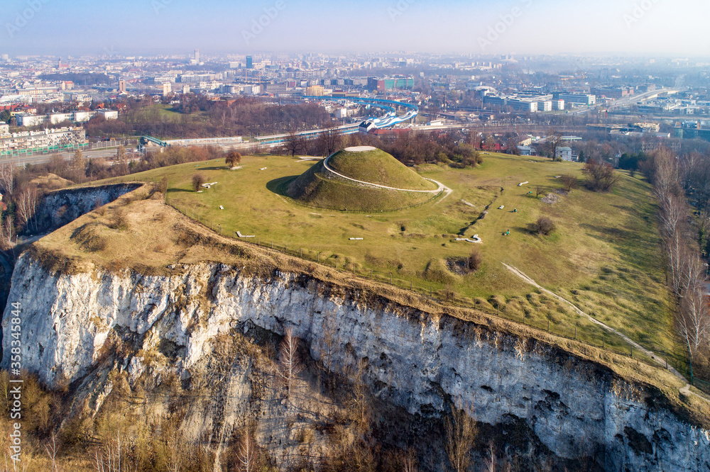 Krakus Mound, Kopiec Krakusa commemorating a legendary founder of Krakow. The origin of the mound, probably early medieval kurgan, is not known. Old quarry in front. City panorama in the background - obrazy, fototapety, plakaty 