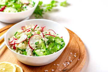 Fresh summer vegetable salad of couscous, radish, cucumbers, parsley and lemon in a bowl on a white background. Vegan food. Spring or summer food. Salad with couscous and raw vegetables, copy space