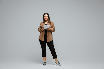 Wall Mural - Fashionable, stylish. Young woman in casual wear on gray background. Bodypositive character, feminism, loving herself, beauty concept. Plus size businesswoman scrolling tablet. Inclusion, diversity.