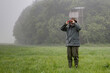 © BIB-Bilder - On a rainy day a hunter stands in front of the hunting pulpit in the meadow and looks through his binoculars.