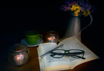 Still life by candlelight black background with open book, pencil and glasses. Concept relaxation, reading, classic, culture