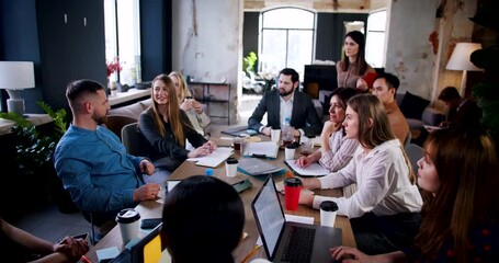 Wall Mural - Teamwork concept. Young male coach speaking to multiethnic business team at modern loft office meeting slow motion.