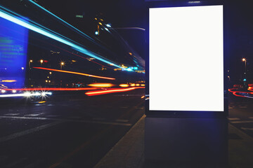 Illuminated blank billboard with copy space for your text message or content, public information board with shutter speed on background, advertising mock up in urban setting, empty poster on roadside