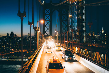 Wall Mural - Metropolitan traffic on Brooklyn bridge with vehicles shining with evening light, yellow cab taxis driving from Manhattan to another district, River crossings, Environmental impact reduction concept