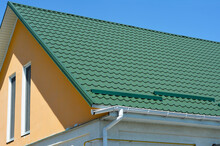 Broken Roof Gutter.  A Close-up On Metal Tiled Gable Roof With Snow Stoppers, Broken Rain Gutter System And Attic Windows Of A House.
