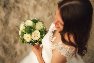 Wall Mural - Top view of attractive brunette bride holding wedding bouquet. White roses flowers. Evening light on sandy beach. Wedding day concept.