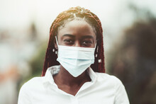 An Outdoor Portrait Of A Young African Female With Chestnut Braids And In A Virus Protective Mask On Her Face; Masked Black Woman Outdoors With Protection Against Influenza And Pandemic Threat