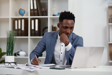 Wall Mural - Businessman with laptop. Young African businessman is typing something on laptop in his office.