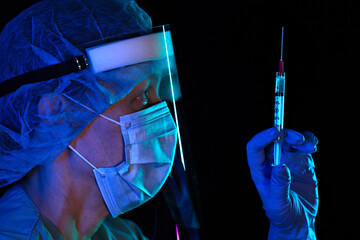 Portrait of female nurse wearing protective mask holding surringe, shallow focus