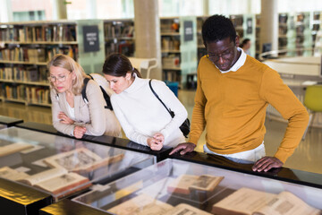 Wall Mural - Professor and adult students read ancient books in a library showcase