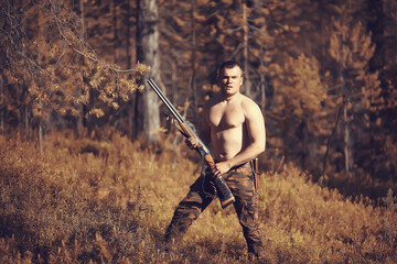 hunting man / hunter with a gun hunting in the autumn forest, yellow trees landscape in the taiga