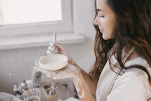 Young Beautiful Woman With Long Curly Hair In White Apron Creating Handmade Ceramic Bowl In A Pottery.