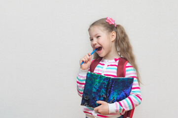 Back to school. Portrait of a blonde schoolgirl standing with book (Notepad) in her hands. The girl is smiling. Light gray studio background. Education. Day of knowledge. copy place