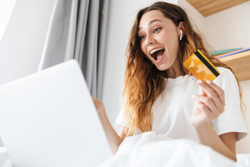 Poster - Portrait of excited woman and holding credit card while using laptop