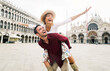 Beautiful couple in love having fun embracing and laughing doing piggyback ride at holiday in Venice, Italy on Piazza San Marco.