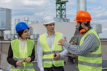 Good looking multiethnic group of workers in a modern building construction site analyzing the plan of construction they wearing the safety helmets