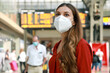 Leinwandbild Motiv Traveler woman wearing KN95 FFP2 face mask at the airport. Young caucasian woman with behind timetables of departures arrivals waiting worried information for her flight.