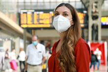 Traveler Woman Wearing KN95 FFP2 Face Mask At The Airport. Young Caucasian Woman With Behind Timetables Of Departures Arrivals Waiting Worried Information For Her Flight.