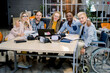 © sofiko14 - Inclusion in work, business team concept. Handsome male coworker on wheelchair with his creative business colleagues in meeting room at creative office, smiling, looking at camera, hugging each other