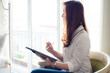 © themorningglory - Happy asian businesswoman using digital tablet sitting on sofa in bedroom over curtain background