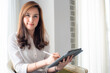 © themorningglory - Happy asian businesswoman using digital tablet sitting on sofa in bedroom over curtain background