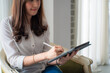 © themorningglory - Happy asian businesswoman using digital tablet sitting on sofa in bedroom over curtain background