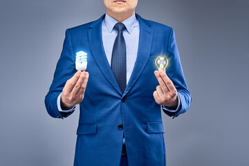 a businessman in a blue suit on a gray-blue background holds two burning light bulbs of different co