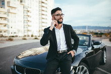 Businessman With Glasses Talking On The Phone Outside A Convertible Car.