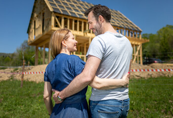 Happy couple outdoor looking at their new home house under construction