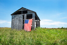 American Flag Hanging Outdoors On Side Of Old Gray Wooden Barn On Grass Hill In United States Rural Countryside.