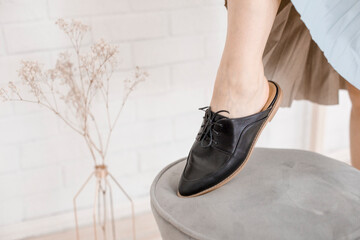 black leather shoes on female legs, a girl resting on a sofa in a blue skirt and with flowers in her hands