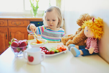 Wall Mural - Adorable toddler girl eating fresh fruits and vegetables for lunch