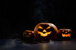 © Михаил Решетников - Three creepy halloween steaming pumpkins with a carved luminous smirk on a black background. A handmade jack-o-lantern head with a candle inside in the dark among the fog. Trick or treat. Postcard.