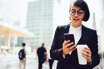 Wall Mural - Smiling female manager surprised with getting discount of email holding blank coffee cup outdoors, prosperous businesswoman enjoying break sending messages on mobile standing on publicity area.