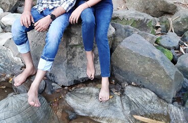 Canvas Print - Barefoot man and a woman with jeans sitting next to each other on big stones