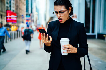 Wall Mural - Emotional female owner of company shocked about getting bad news on email strolling on street, stressed businesswoman angry about problems with project checking web site information on phone.