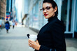 © BullRun - Portrait of confident businesswoman with red lips holding coffee to go standing near copy space area for advertising, serious female manager in elegant wear looking at camera walking on street.