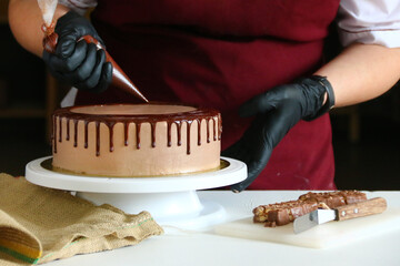 Wall Mural - liquid chocolate on cake. A confectioner squeezes liquid chocolate from a pastry bag on to a cream biscuit cake with background