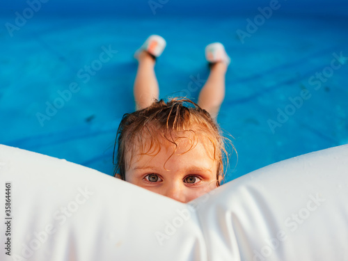 Fotografía Young girl lying in pool and hiding her face looking at camera