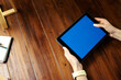 © Rymden - Mockup image of a woman using digital tablet with blank screen on wooden table. Close up photo of female hands holding device horizontally
